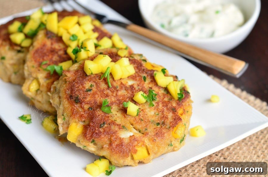 3 Spicy Mango Crab Cakes on a plate with diced mango and parsley and a fork 