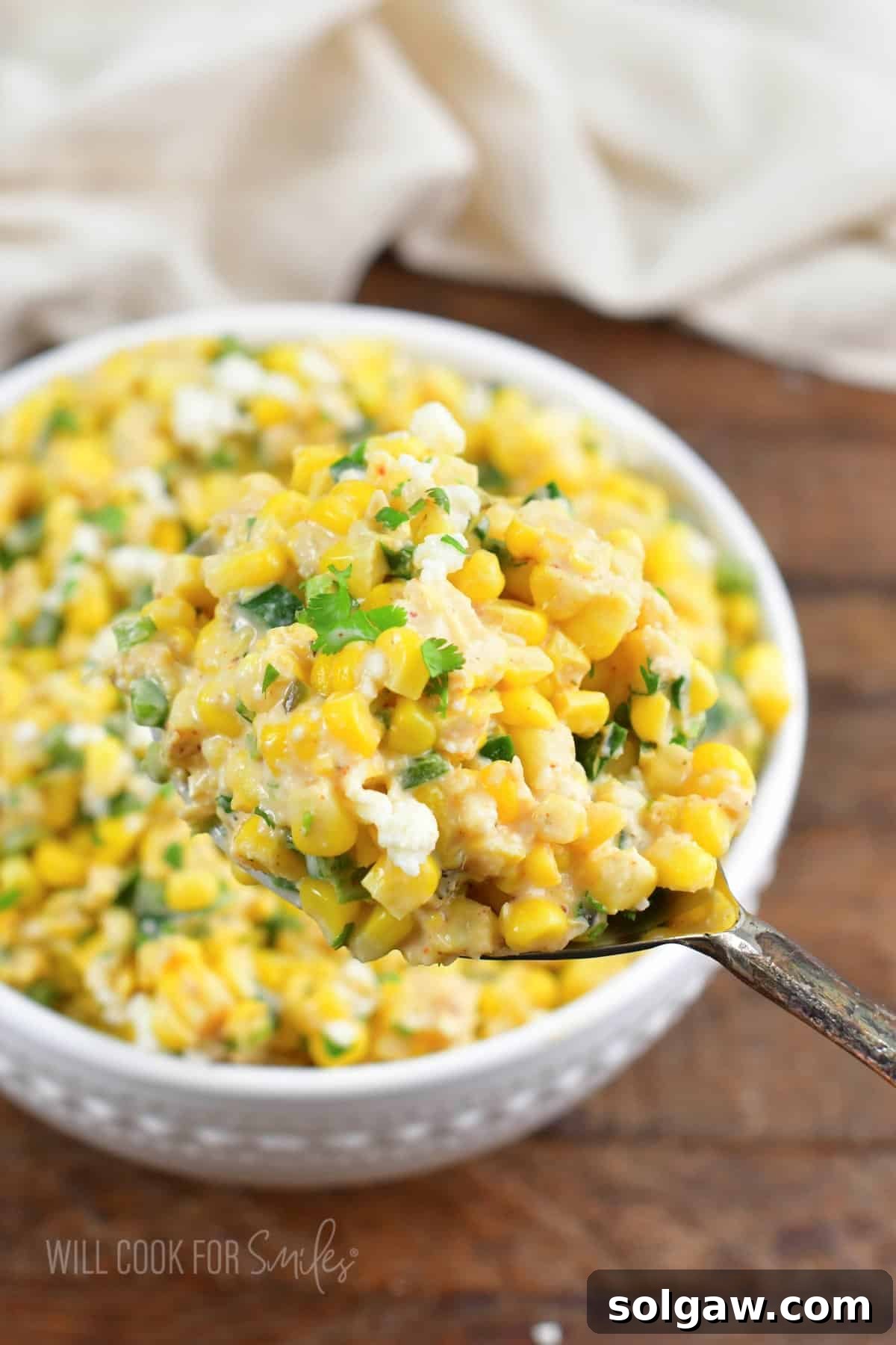 scooping out some creamy Mexican street corn salad with a large spoon.