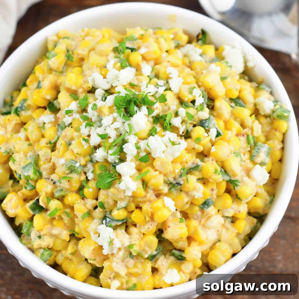 creamy Mexican corn salad in a white bowl topped with crumbled queso.