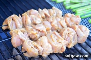 Orange Glazed Chicken Skewers 7 Skewering rolled chicken thigh pieces onto a metal skewer for grilling.