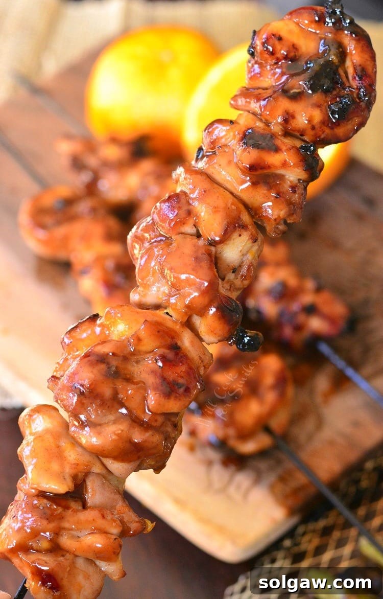 Orange Glazed Chicken Skewers 3 A hand lifting a glistening Sticky Orange Chicken Kebab from a stack on a cutting board, emphasizing its sticky glaze and tenderness.