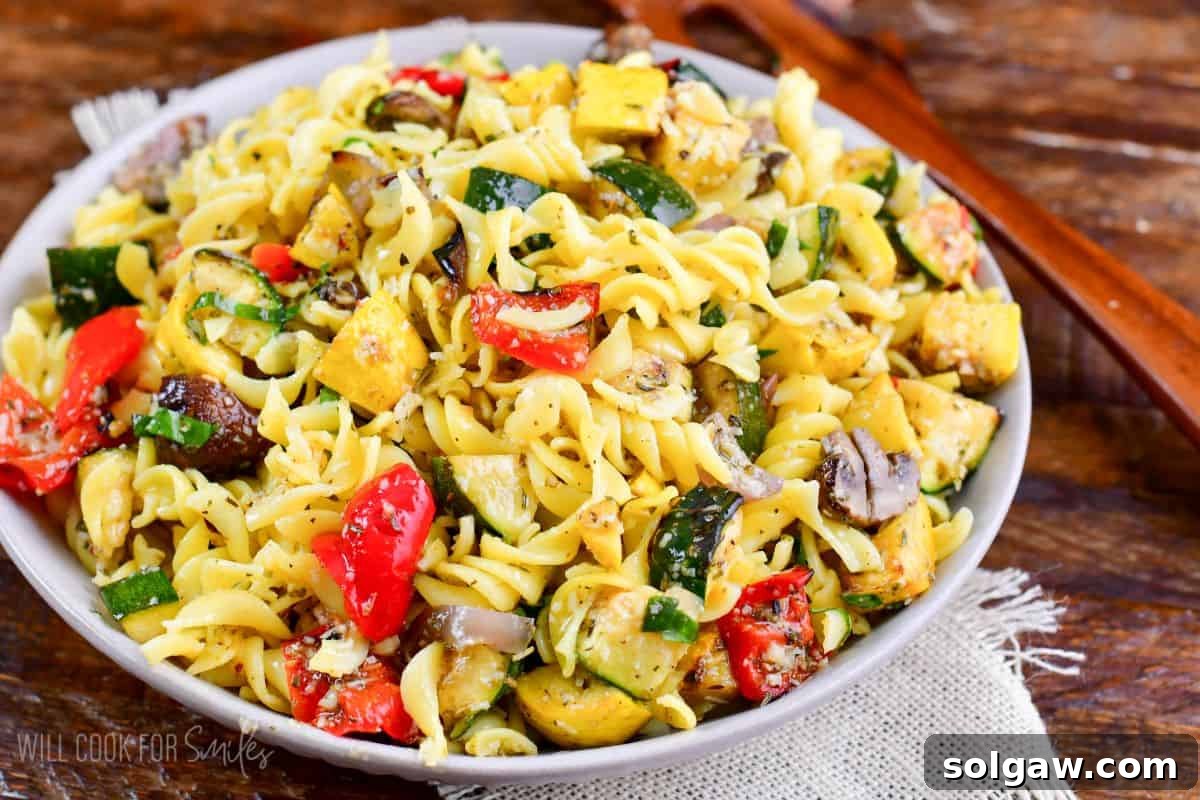 Smoky Grilled Veggie Pasta Salad 7 Grilled vegetable pasta salad in a white bowl with a wood spoon resting on the side.
