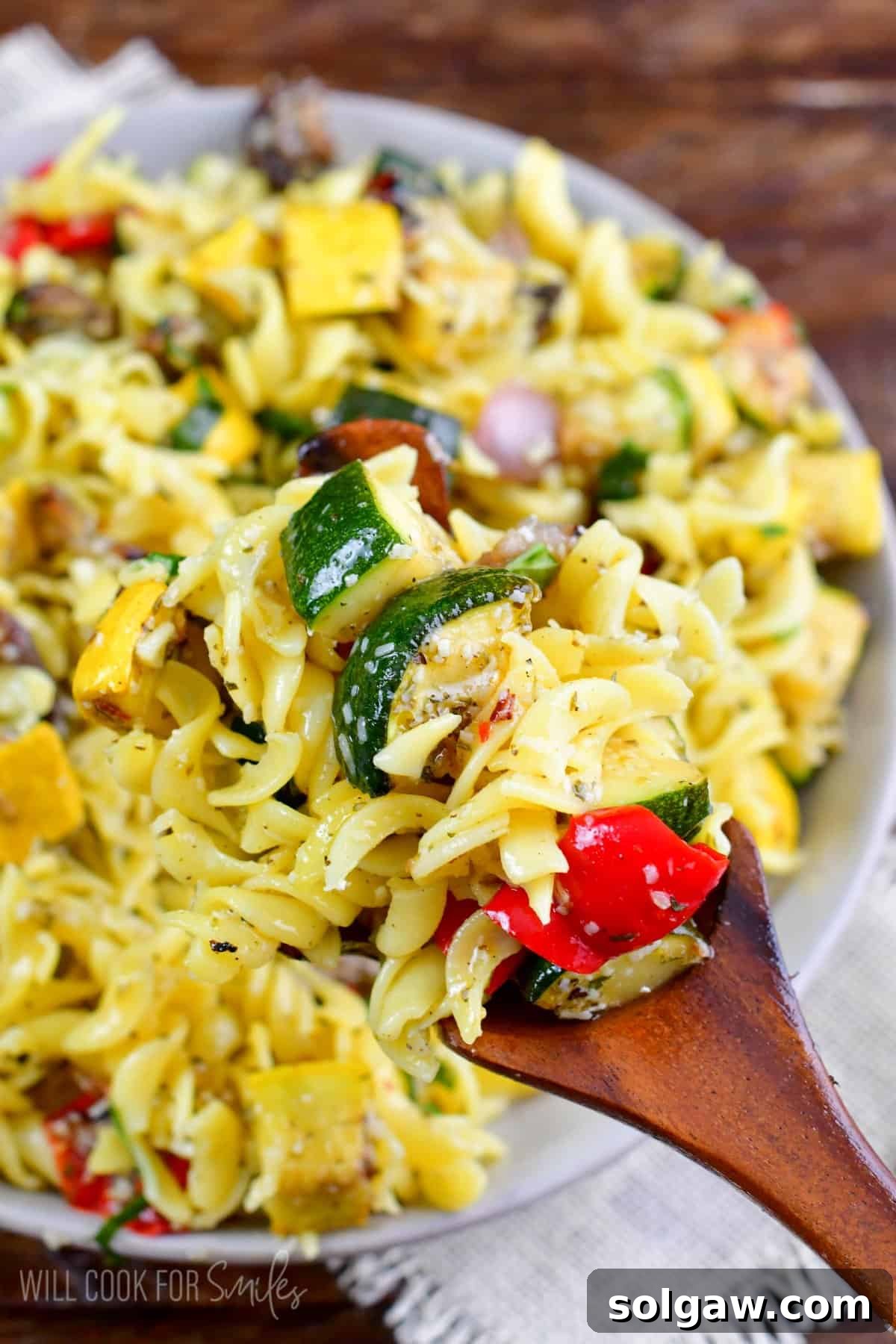 Smoky Grilled Veggie Pasta Salad 8 Scooping up some grilled pasta salad with a wooden spoon from a large bowl.