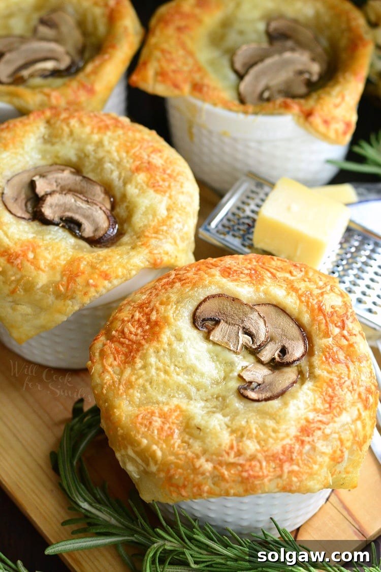 Individual Creamy Chicken and Mushroom Pot Pies with rosemary on a cutting board with cheese on top of a cheese grater on a wood cutting board 