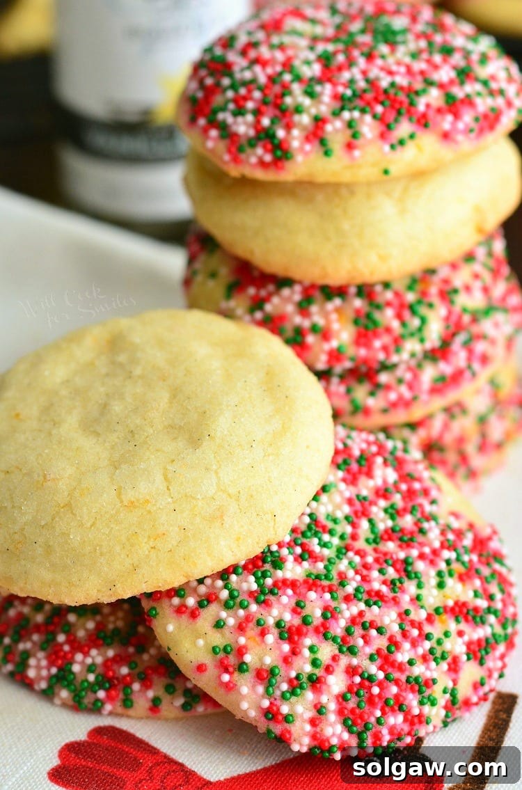 Zesty Orange & Vanilla Bean Sugar Cookies 6 Several sugar cookies with orange and vanilla flavors, some adorned with festive sprinkles, stacked on a plate.