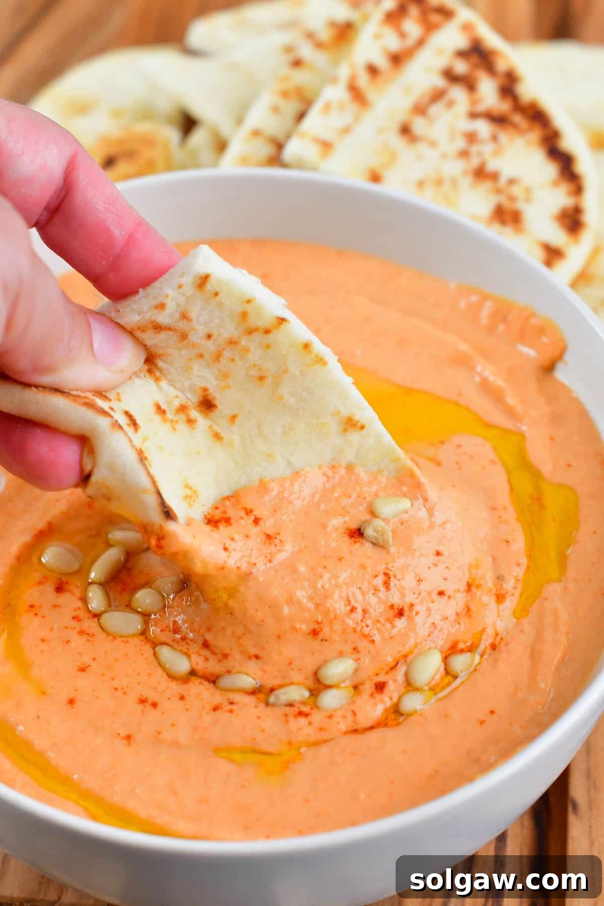 Vibrantly red roasted bell pepper hummus in a bowl, garnished with a swirl of olive oil and a sprinkle of paprika.