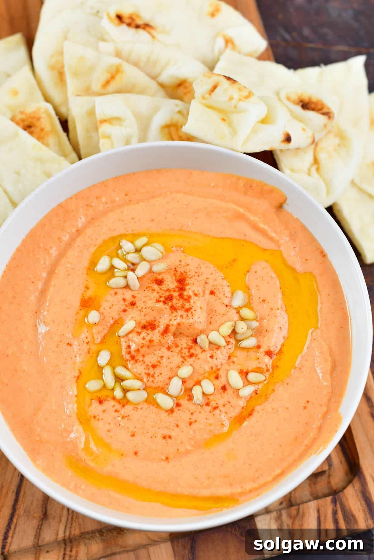 Top view of roasted red pepper hummus in a bowl, garnished with pine nuts and served with warm na'an bread for dipping.