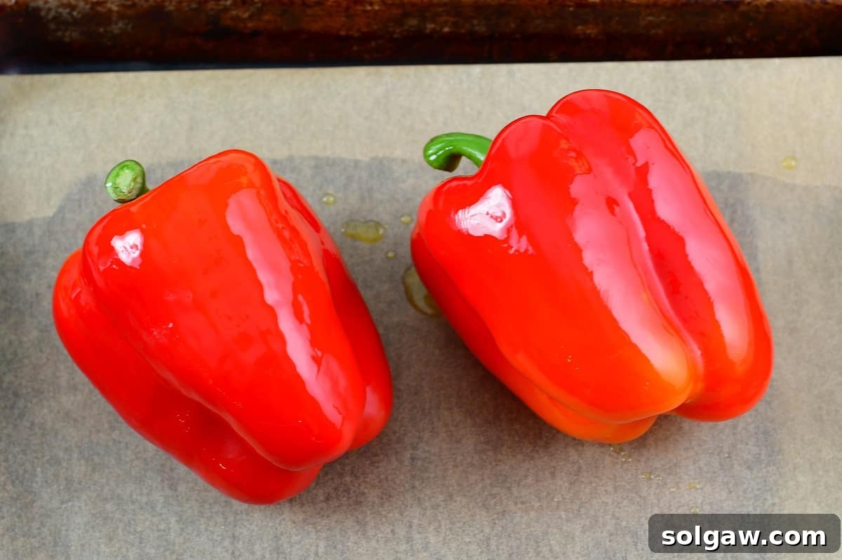 Two fresh red bell peppers arranged on a baking sheet, ready for roasting.