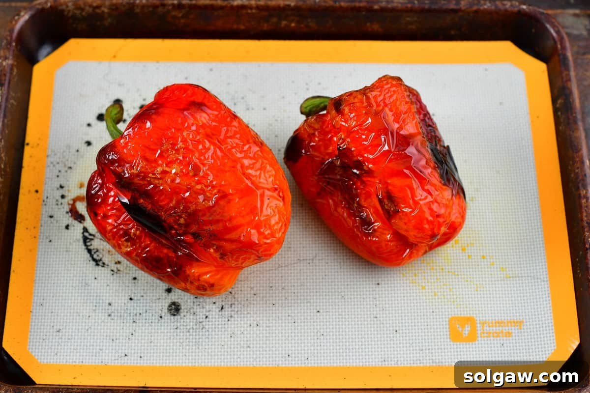 Perfectly roasted red bell peppers with blistered and charred skin on a baking sheet, fresh out of the oven.