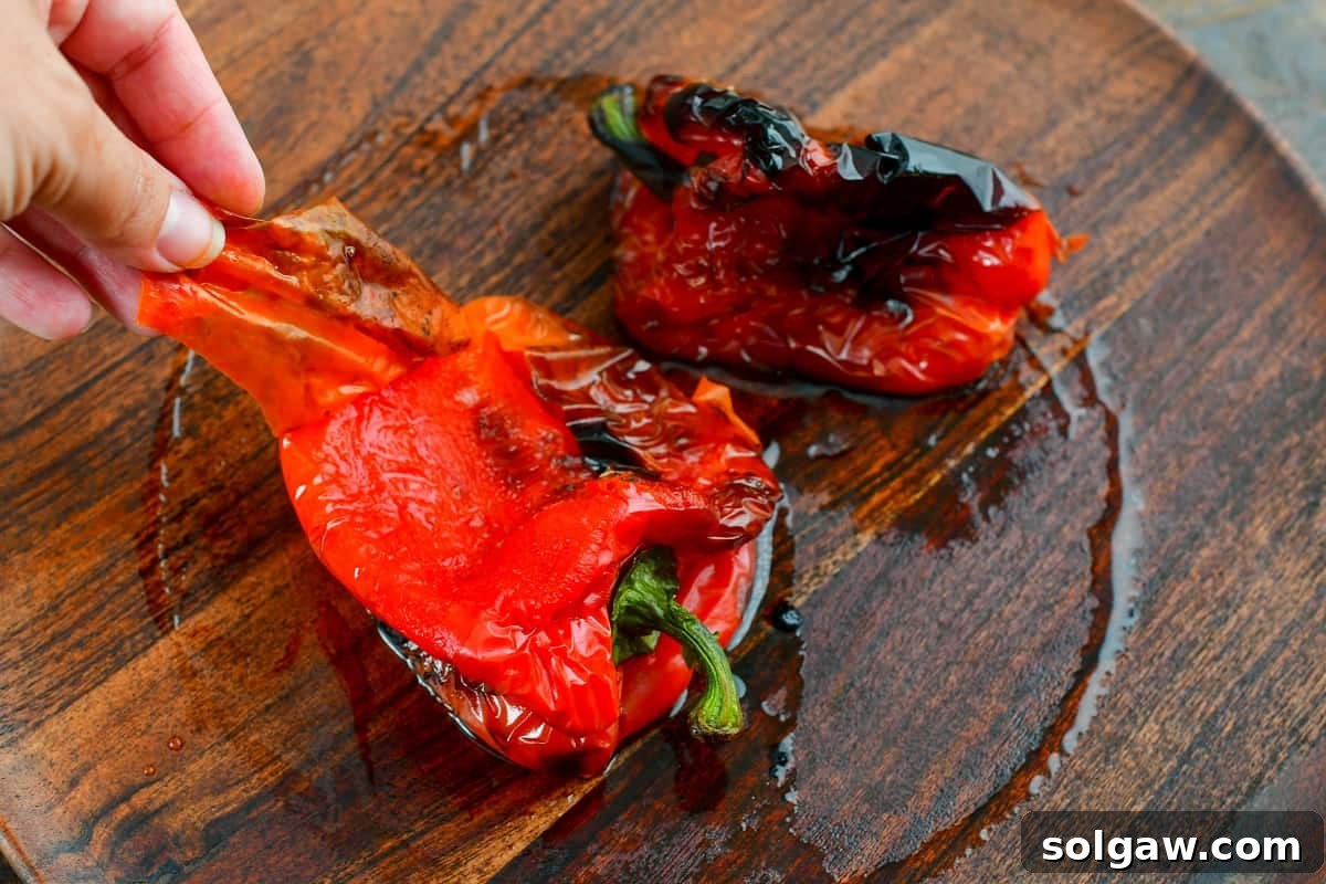 Hands carefully peeling off the charred skin from a roasted red bell pepper.