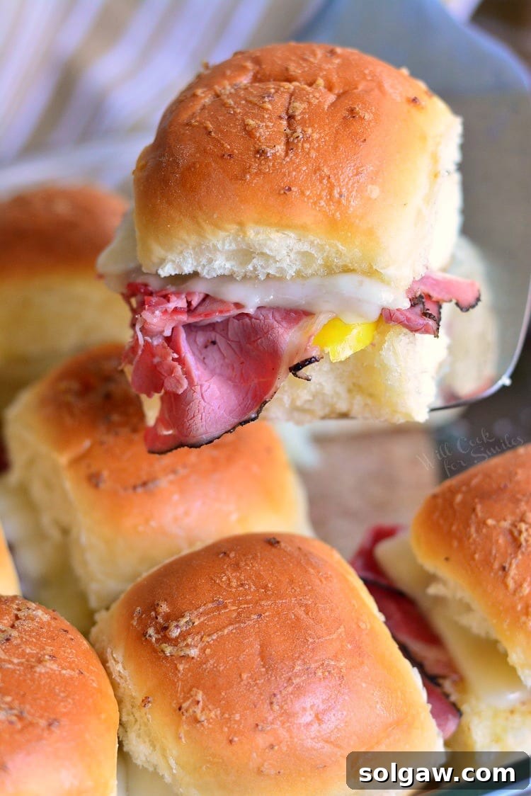 Hot Pastrami Sliders on a baking sheet with one being lifted out with a spatula