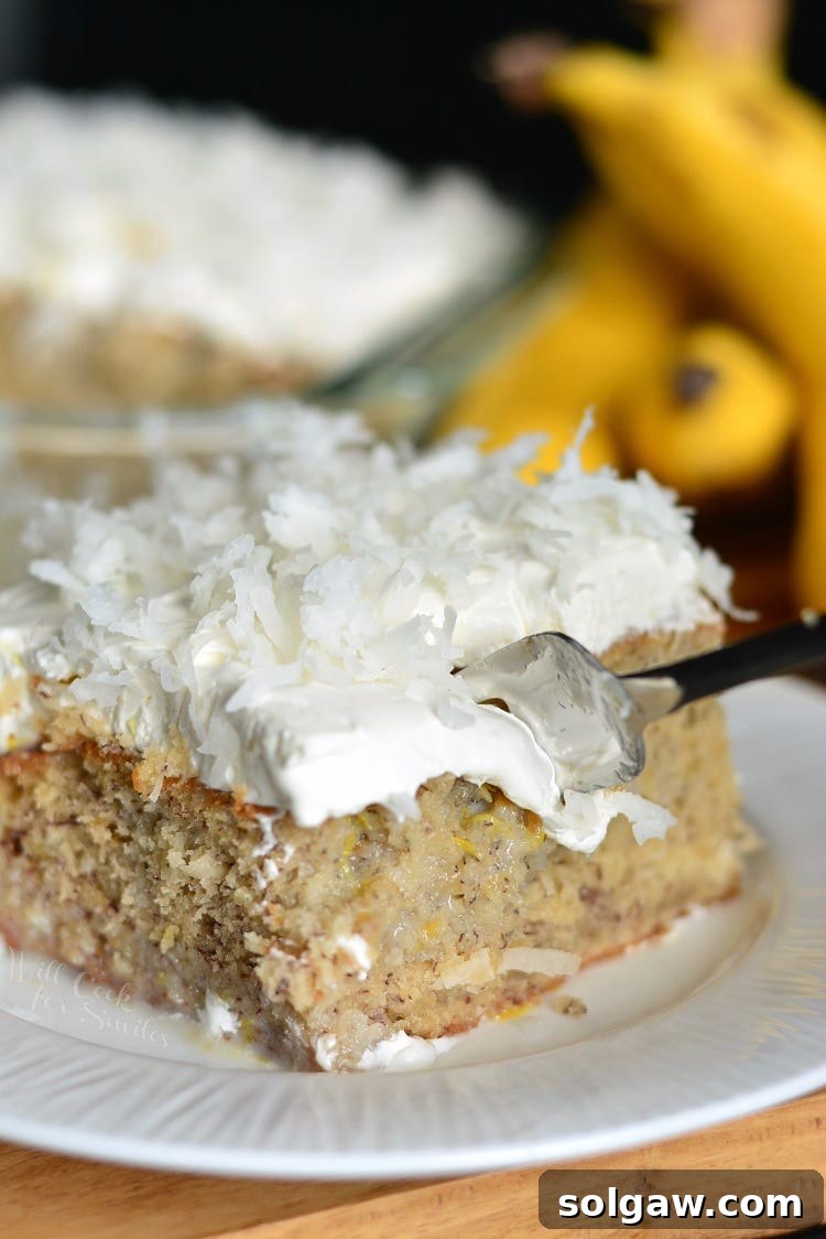 A slice of Lemon Coconut Banana Poke Cake with a fork, showing its moist texture