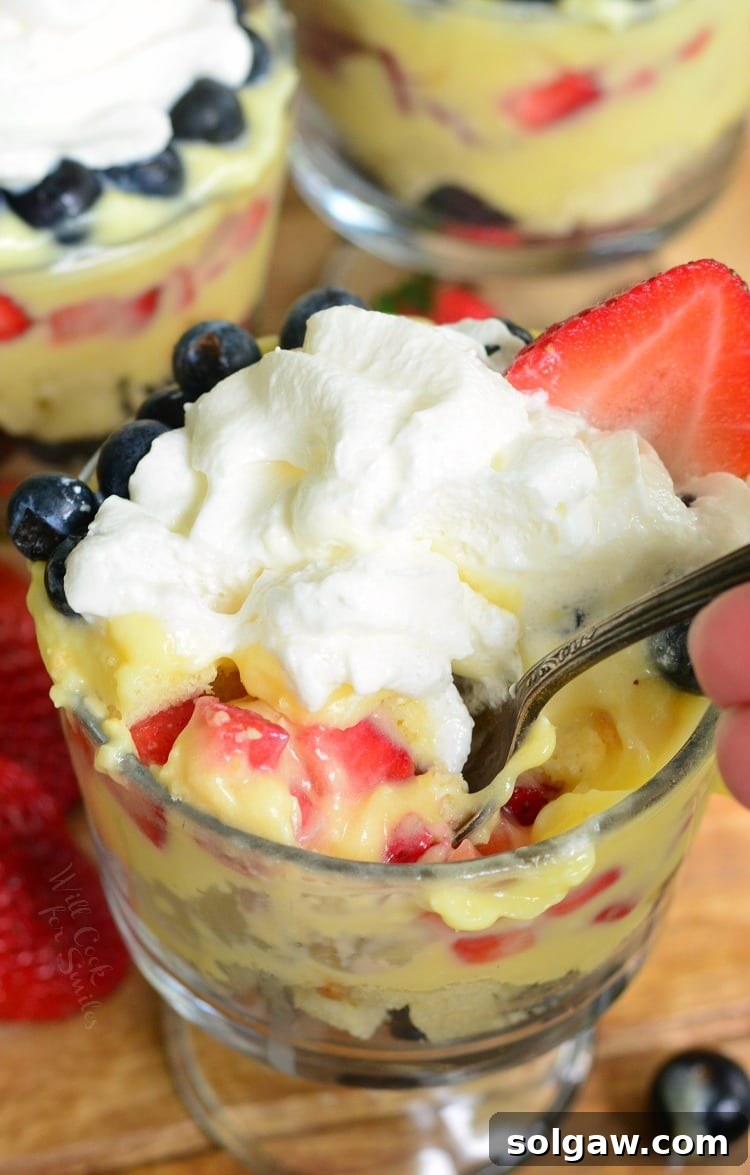 Easy Coconut Berry Trifle in a glass serving bowl with a spoon on a cutting board with a strawberries