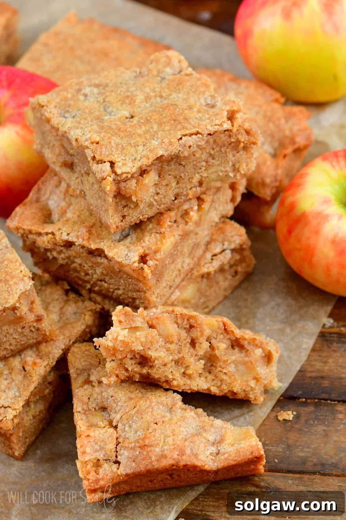 Chewy Spiced Apple Blondie Bars 2 Stacked apple pie blondies, one broken in half to show the soft interior, resting on wax paper amidst whole apples.