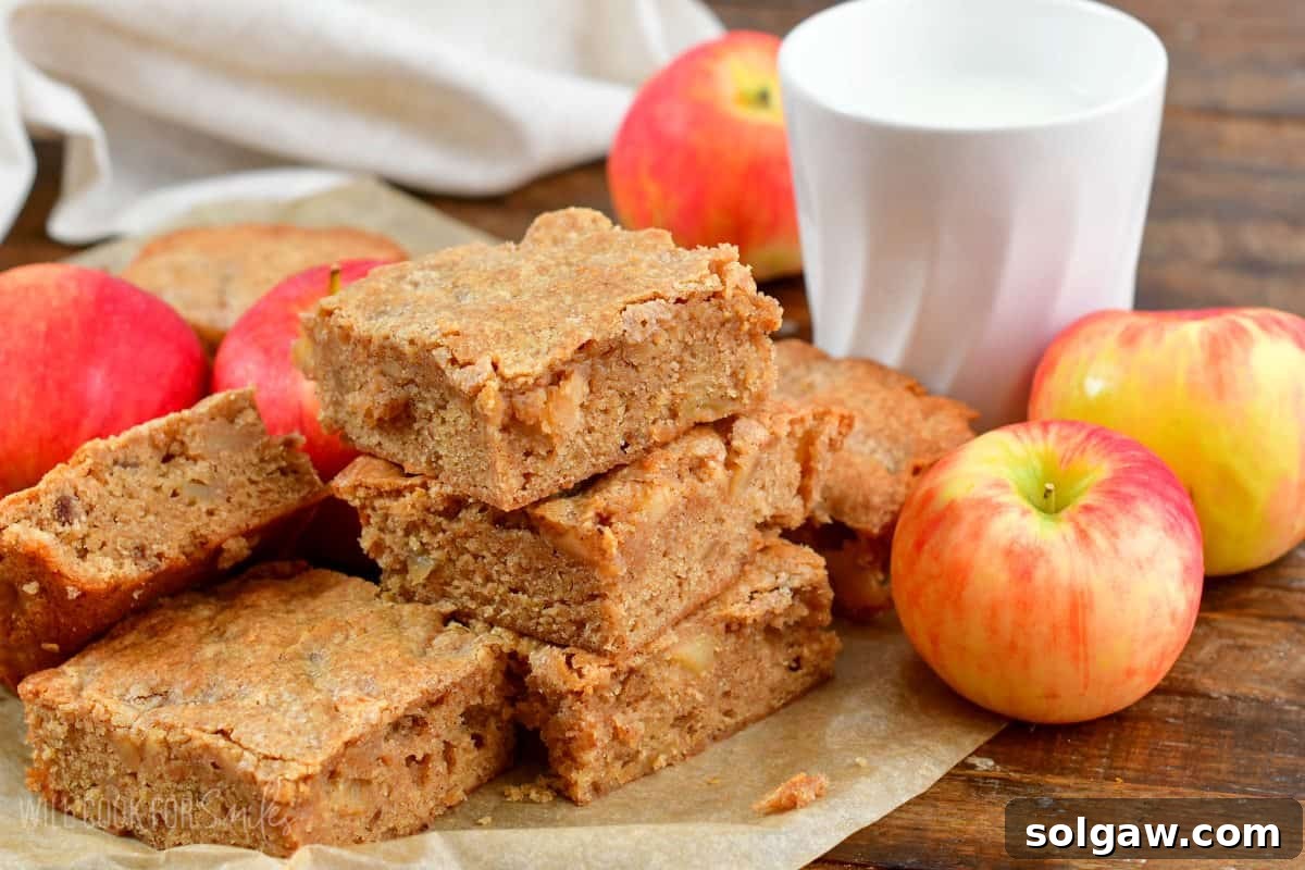 Chewy Spiced Apple Blondie Bars 6 Slices of apple pie blondies stacked on wax paper, surrounded by fresh apples.