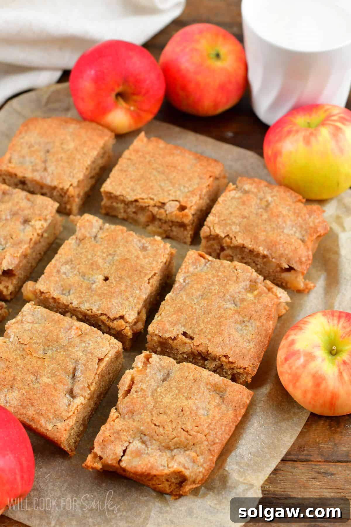 Chewy Spiced Apple Blondie Bars 7 Sliced apple pie blondies arranged on parchment paper with whole apples in the background.