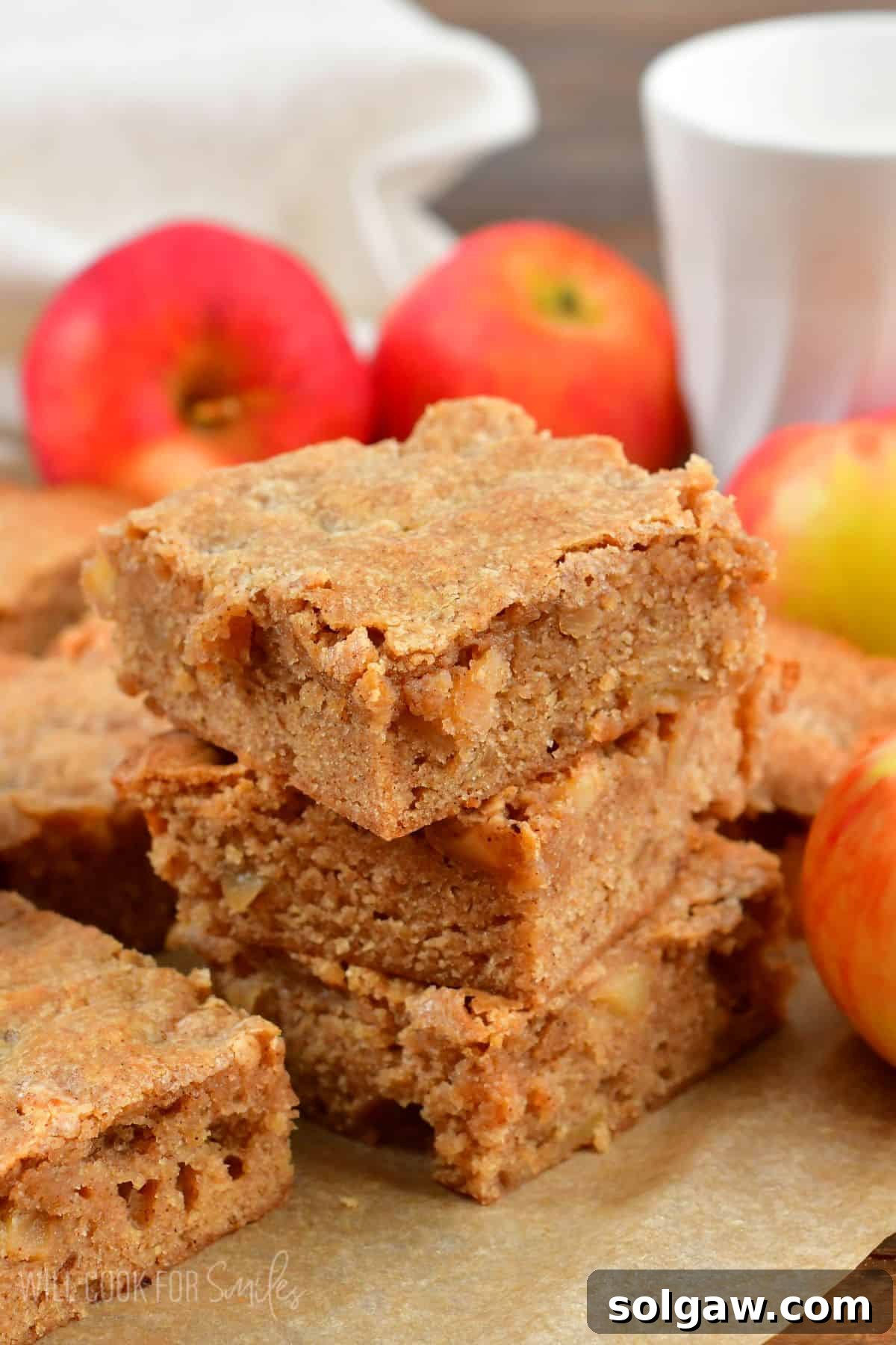 Apple pie blondies stacked up on wax paper with apples in the background.