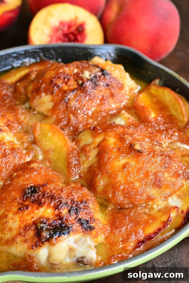 Four chicken thighs with a glistening ginger peach sauce and fresh peach slices in a rustic green cast iron pan, with whole peaches artfully arranged in the background.