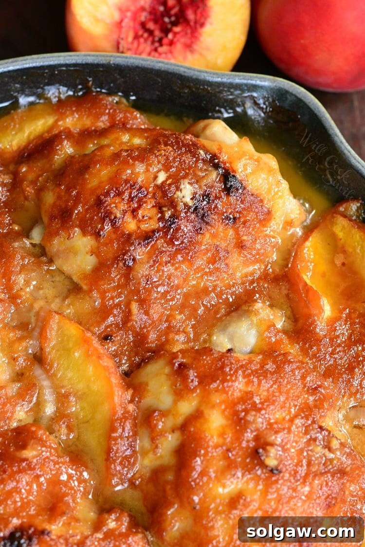 Close-up horizontal view of two perfectly baked chicken thighs glistening with ginger peach sauce, surrounded by caramelized peach slices in a green cast iron pan, ready to be served.