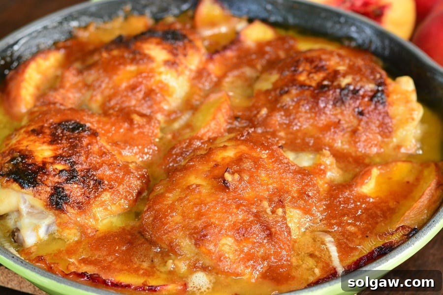A horizontal view showcasing four golden-brown chicken thighs coated in a sweet and savory ginger peach sauce, nestled with peach slices in a green cast iron pan, fresh out of the oven.
