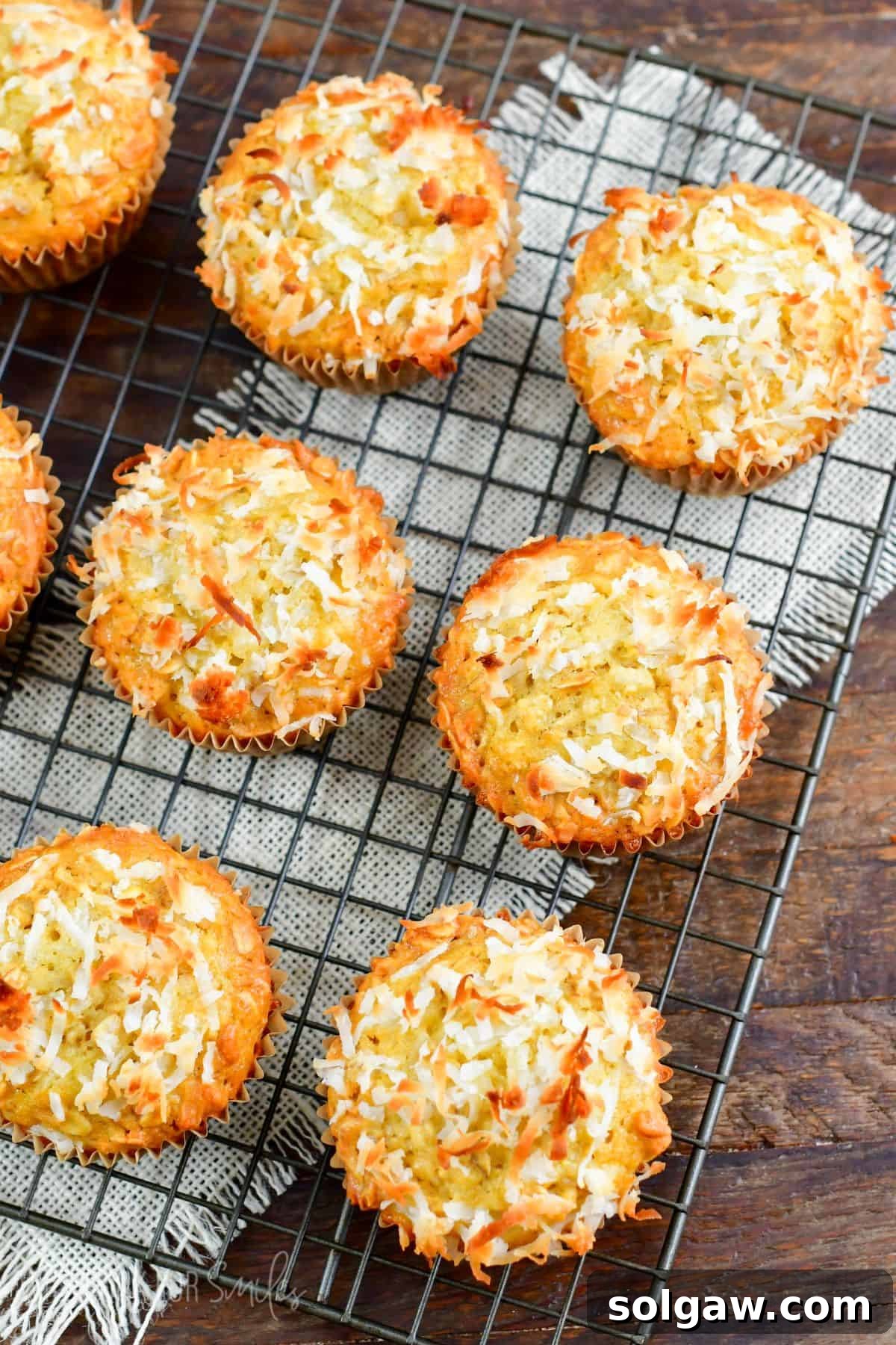 Freshly baked Coconut Oat Muffins cooling on a wire rack, placed on a rustic wood surface with a white burlap cloth underneath.