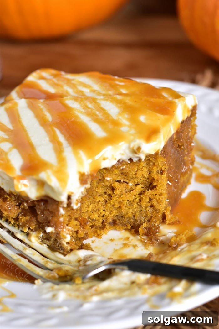 A top-down view of a rectangular salted caramel pumpkin cake, frosted with cream cheese frosting and drizzled with more caramel. The cake is soft and moist, with a rich orange color. There are slices already cut, revealing the internal texture.