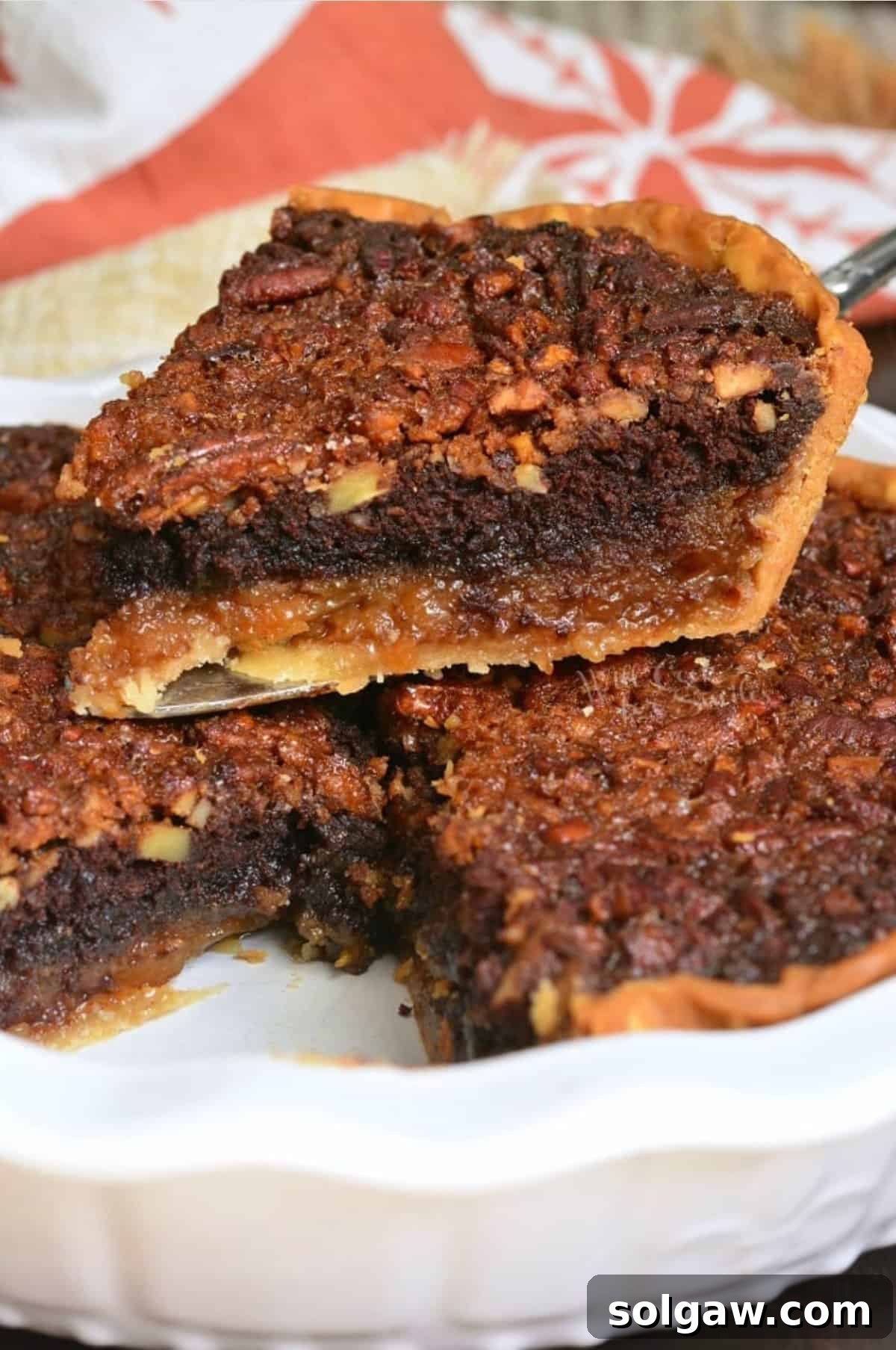 A slice of irresistible Brownie Pecan Pie served on top of the whole pie in a pie dish, showcasing its distinct layers.