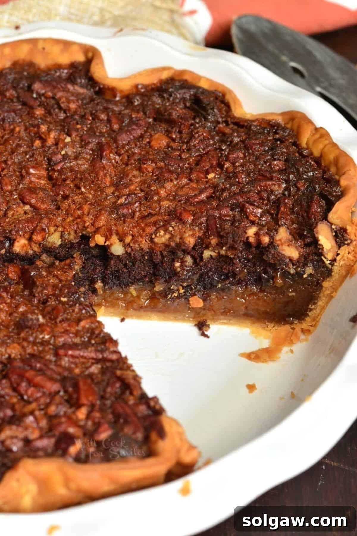 A whole Brownie Pecan Pie in its baking dish, with one perfect slice removed to show the interior layers.
