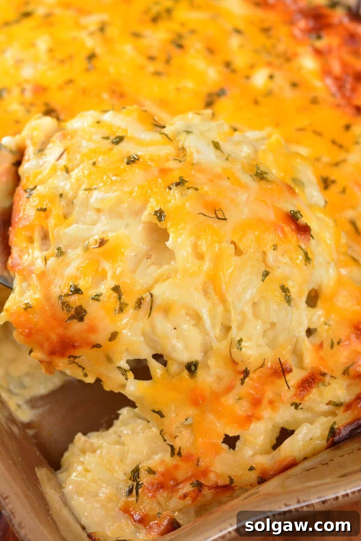 Beginning to scoop out a portion of gooey, cheesy potato casserole from the baking dish, showing the melted cheese pull.