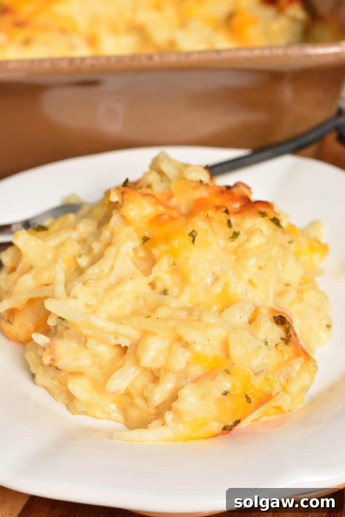 A serving of hashbrown casserole on a white plate with a fork, ready to be enjoyed.