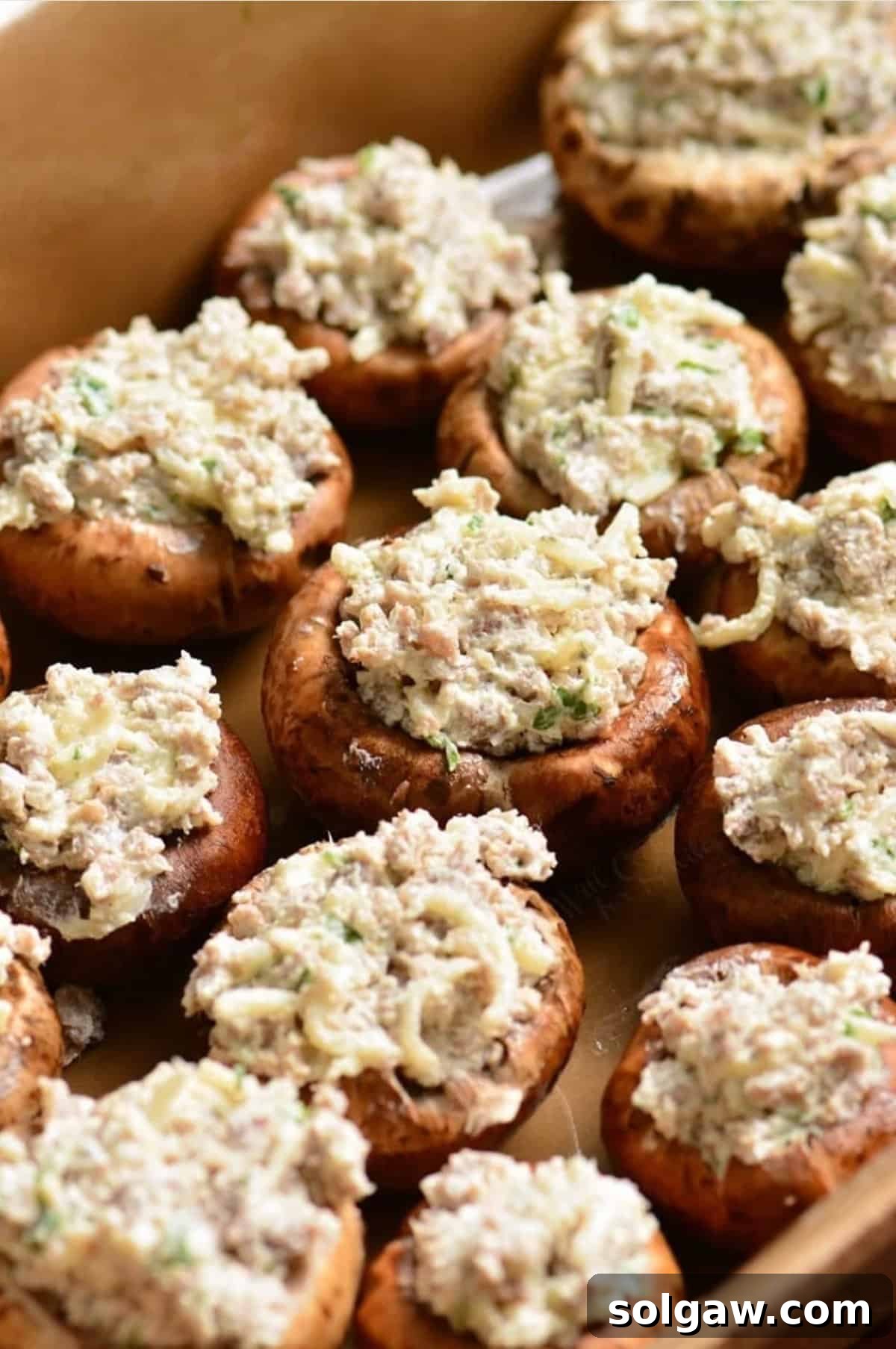 Mushrooms stuffed with savory sausage filling arranged on a baking dish, ready for the oven.