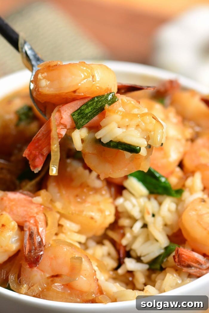 Zesty Garlic Shrimp Rice Bowl 5 A fork lifts juicy shrimp and scallions from a garlic shrimp rice bowl.