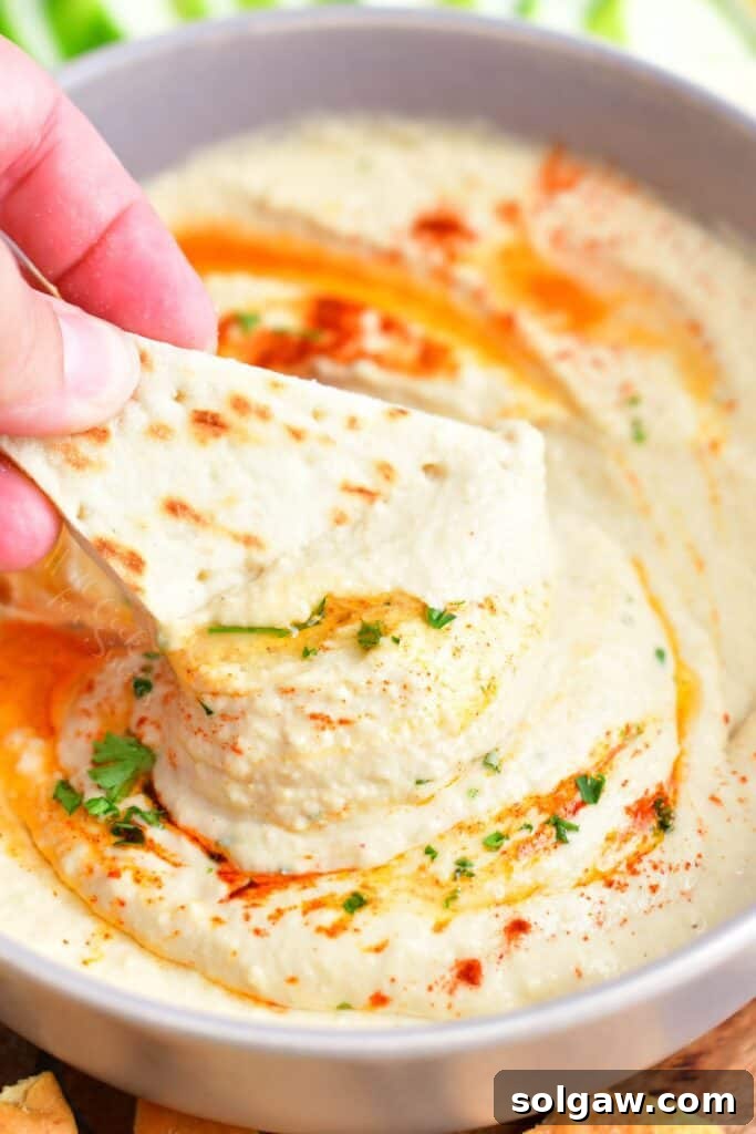 A piece of naan is being dipped into hummus.