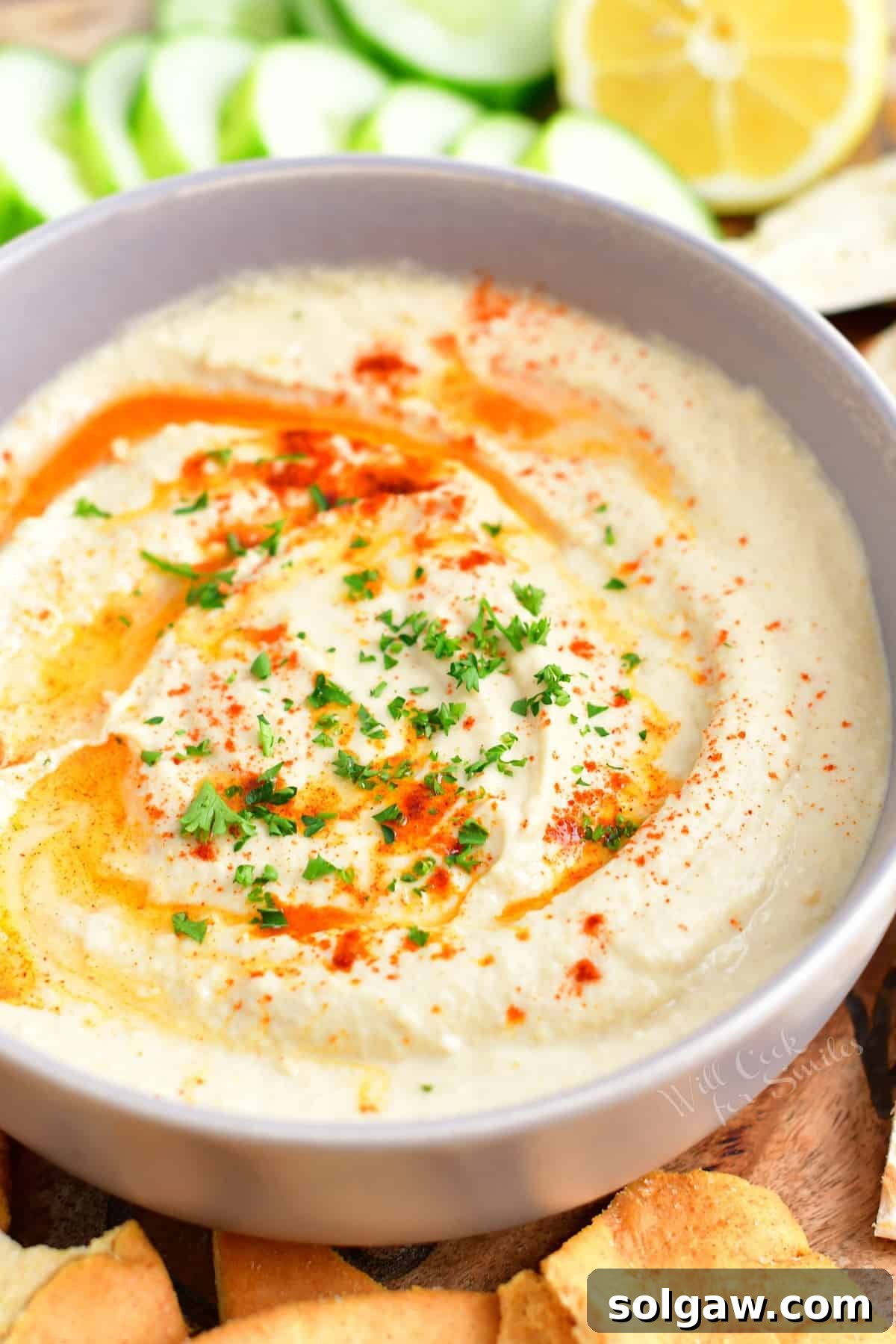 A white bowl filled with hummus is ready to be eaten.
