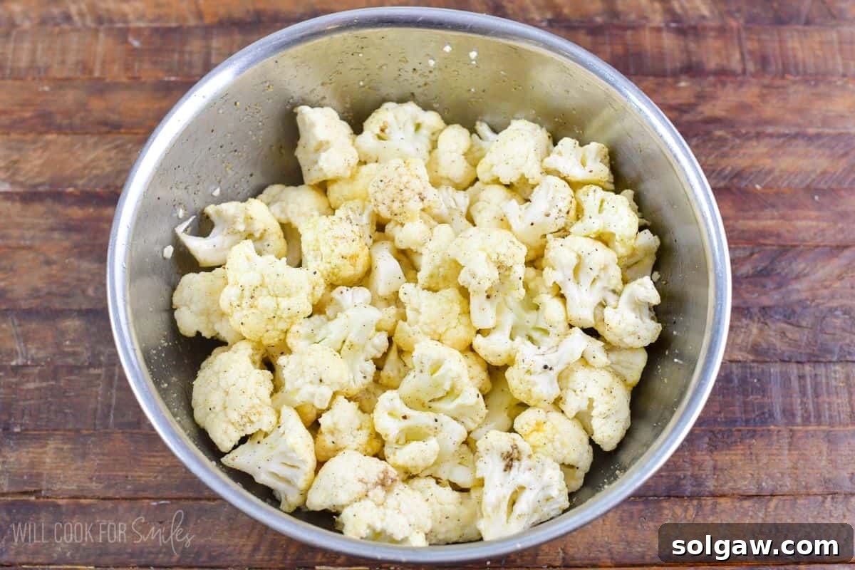 Chopped cauliflower florets mixed with seasoning in a mixing bowl, ready for roasting.