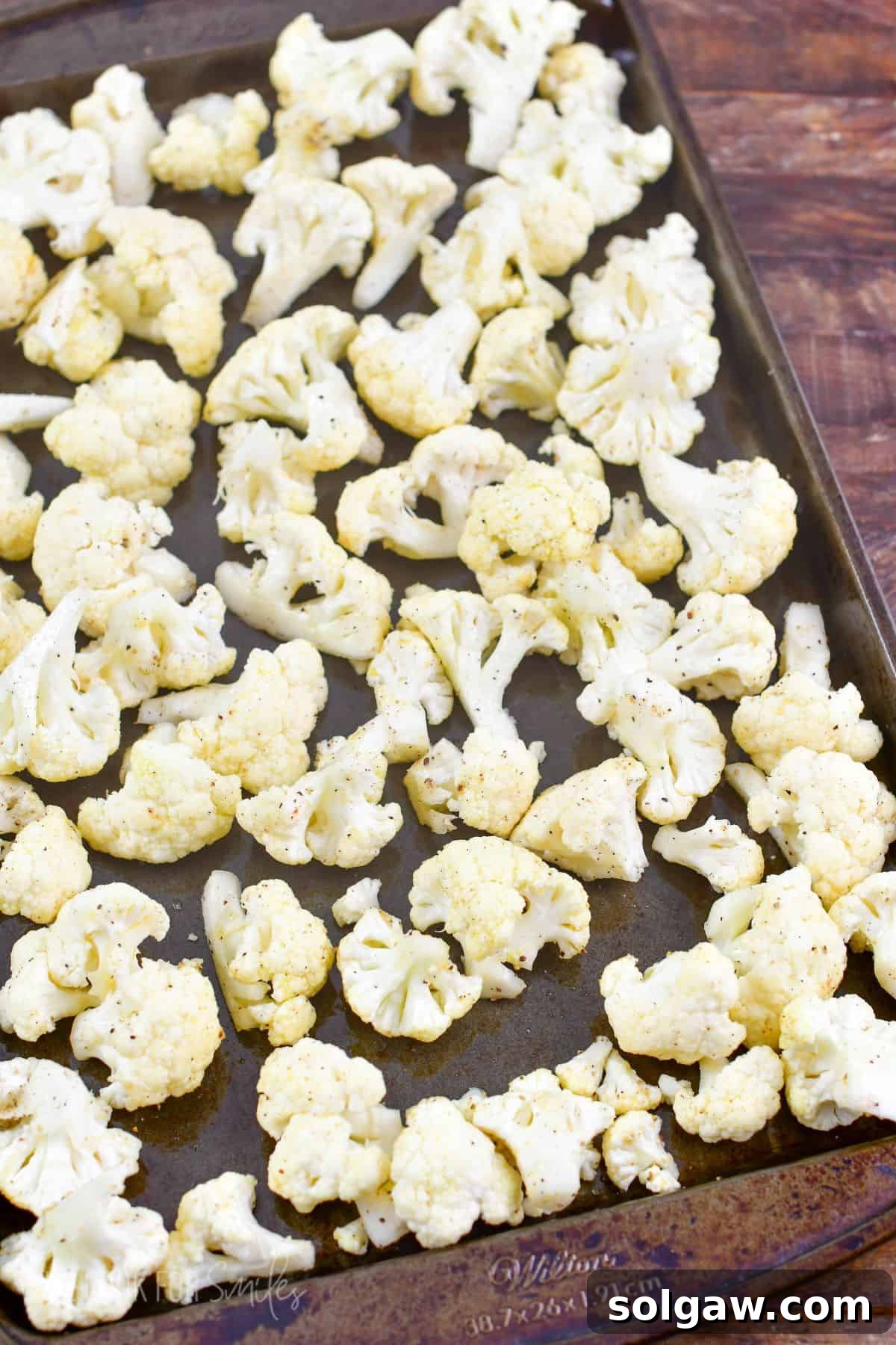 Uncooked seasoned cauliflower spread on a baking sheet in a single layer.