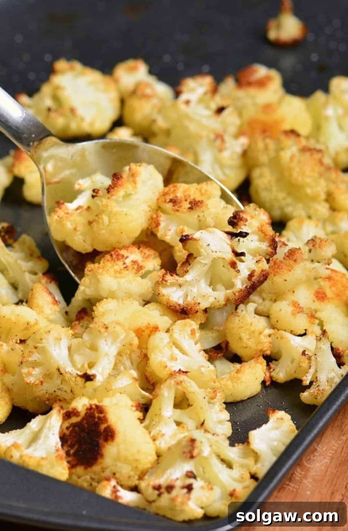 Roasted cauliflower on a baking sheet with a spoon scooping some up, showing its golden color.