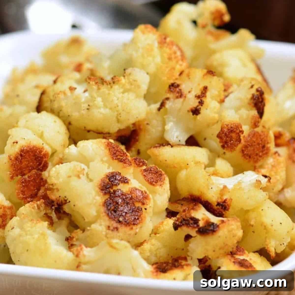 Roasted pieces of cauliflower in a white bowl, garnished and ready to serve.