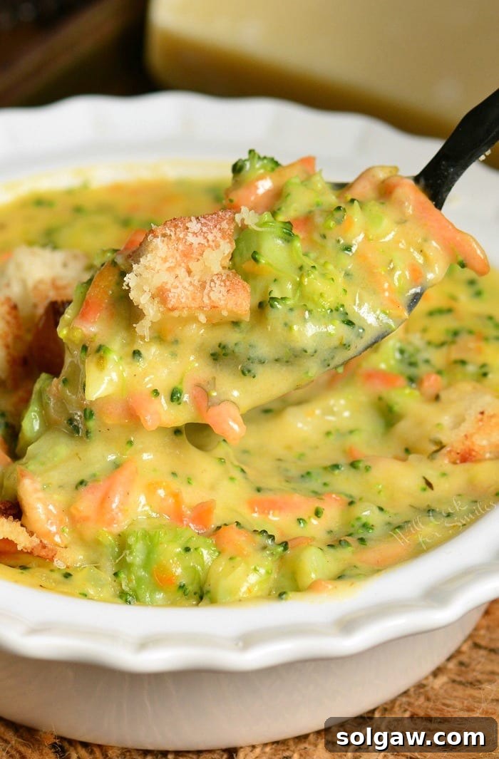 scooping out some creamy and cheesy broccoli soup from a bowl with a spoon.
