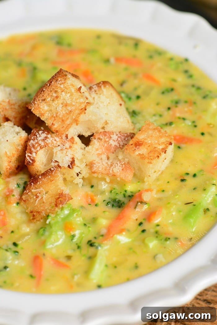 a bowl filled with creamy broccoli cheese soup topped with crispy croutons.