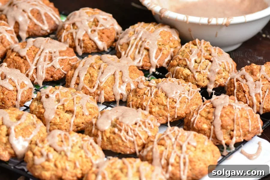 Soft and Chewy Oatmeal Cookies cooling on a wire rack, with a bowl of cinnamon glaze in the foreground.