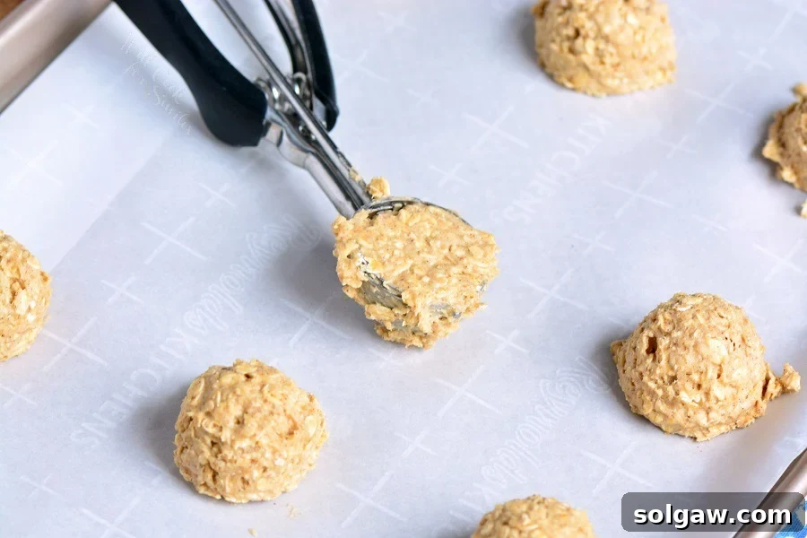 Scooping raw Cinnamon Oatmeal Cookie dough onto parchment paper-lined baking sheet.