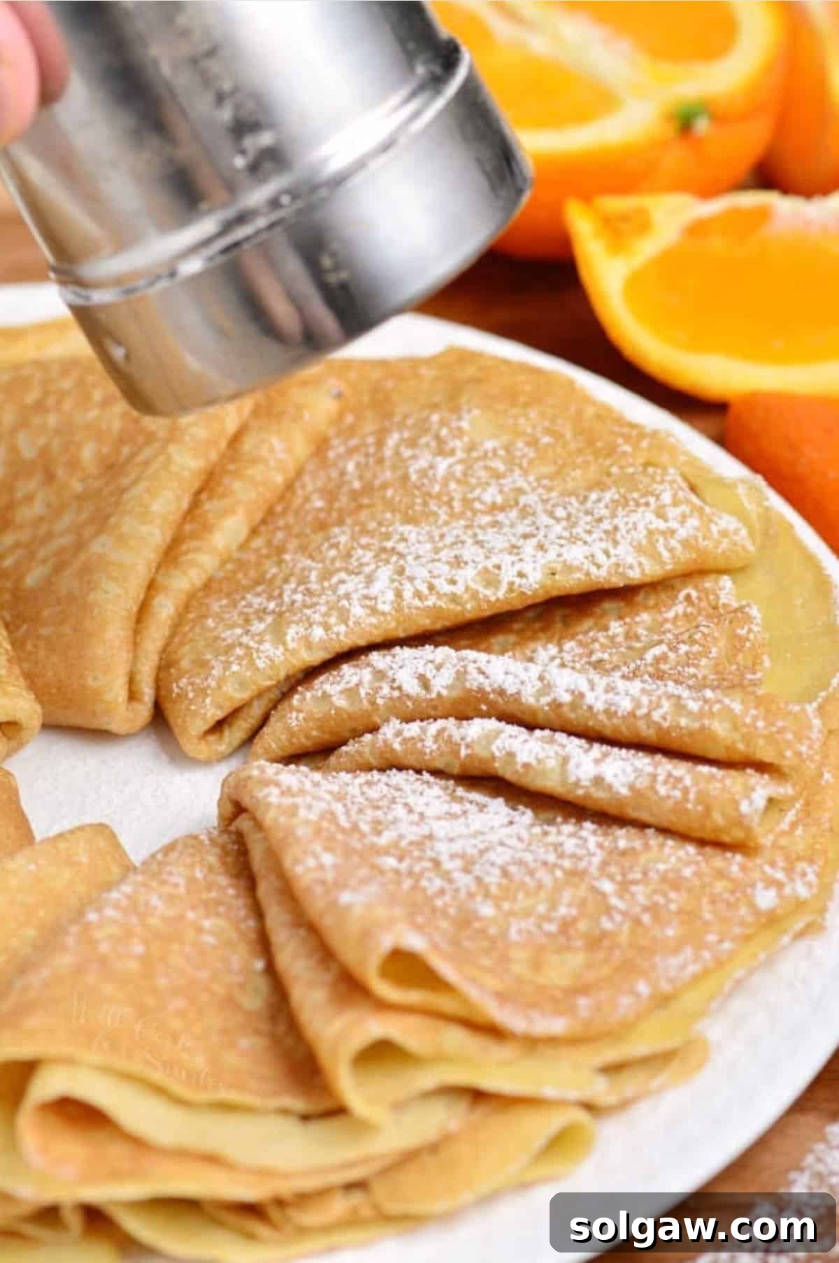 The Art of Perfect Crepes 5 Adding powdered sugar to folded crepes elegantly arranged on a white plate, enhancing their sweetness.