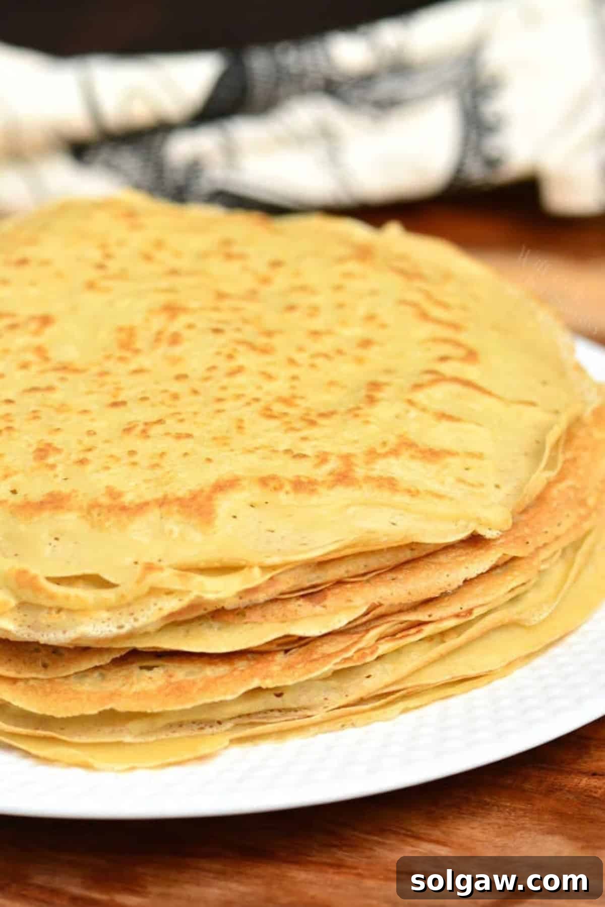 A tall stack of golden crepes on a platter, ready to be served, embodying homemade comfort.
