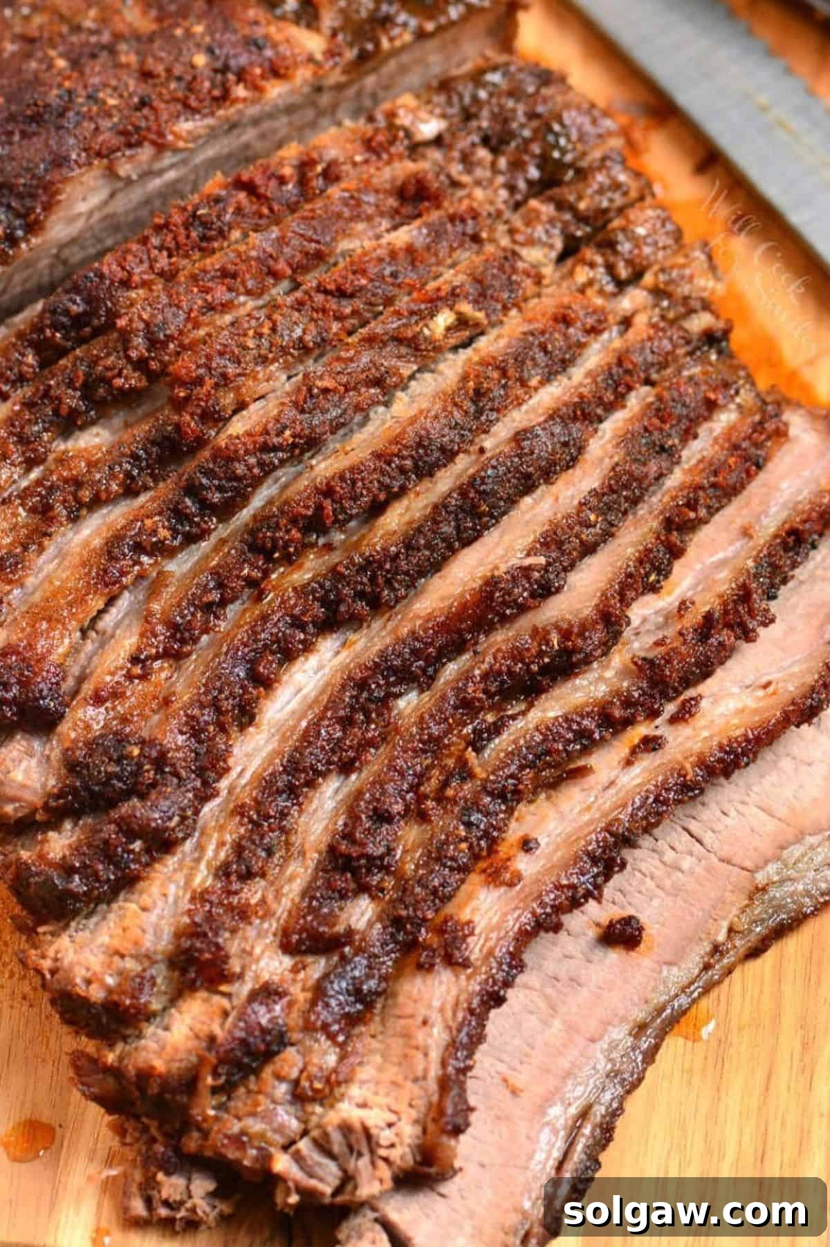 sliced dry rubbed juicy beef brisket laying on the cutting board next to a knife.
