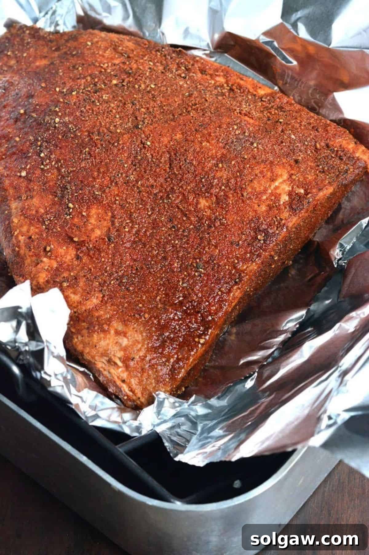 cooked beef brisket flat coated in seasoning in a foil in a roasting pan.