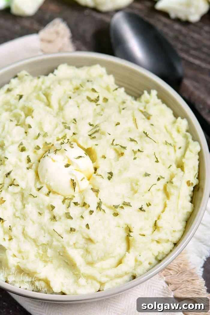 Mashed Cauliflower in a serving bowl with herbs and butter over top 