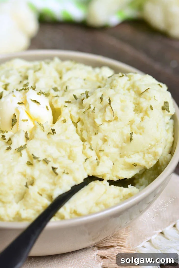 Mashed Cauliflower in a serving bowl with butter and herbs with a serving spoon 