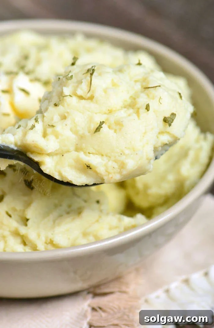 Mashed Cauliflower in a bowl being scooped up with a serving spoon 