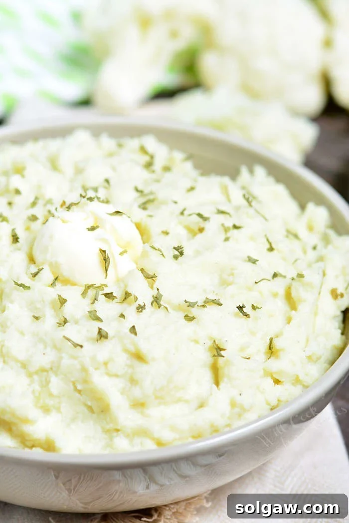 Mashed Cauliflower in a serving bowl with butter and herbs 